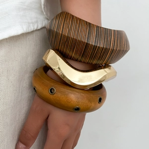 Close-up of stacked vintage wooden bracelets with wavy gold metal and rivet details