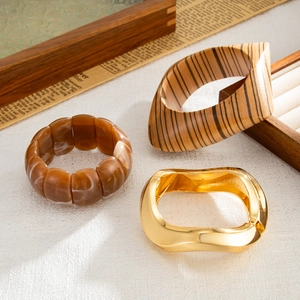 Macro detail of amber resin beads, wood grain cuff, and wavy gold metal bracelet