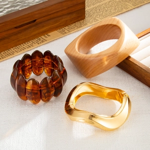 Detail of wooden bangle, resin bead bracelet and gold wavy cuff set on a rustic background