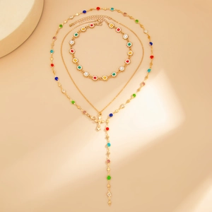 Dettaglio della collana a tre strati dorata con ciondolo a croce e perle colorate