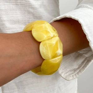 Dettaglio del bracciale in resina marmorizzata gialla al polso su uno sfondo di lino