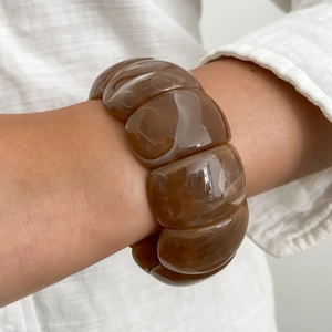 Primo piano di un ampio bracciale in resina spessa con motivo tartarugato marrone scuro al polso