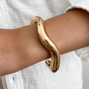 Dettaglio di un bracciale rigido dorato a onde con design organico e minimalista