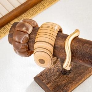 Dettaglio di tre bracciali in resina ambrata, legno naturale e metallo dorato su supporto