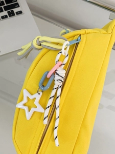 Detailaufnahme der gelben Canvas-Brusttasche mit blauem Reißverschluss und Stern-Anhänger