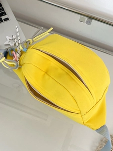 Detail der gelben Canvas-Brusttasche mit bunten Kordelanhängern und Doppelreißverschluss