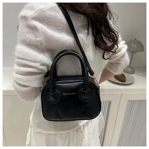 Chic black round crossbody bag with gold text shown on model in minimalist home setting