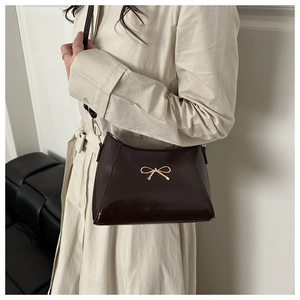 Detail of a glossy dark brown shoulder bag featuring a gold metal bow on beige coat