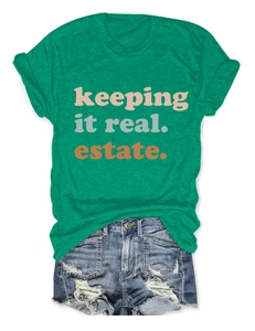 Dettaglio della t-shirt verde con stampa 'keeping it real. estate.' e maniche arrotolate