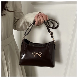 Detail of glossy patent leather handbag featuring a decorative gold metal bow buckle