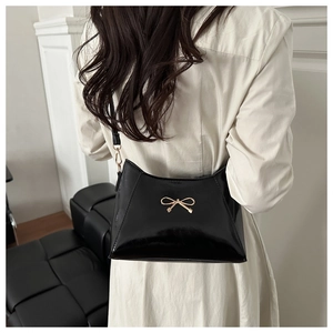 Close-up of elegant black patent handbag with golden bow buckle on beige coat