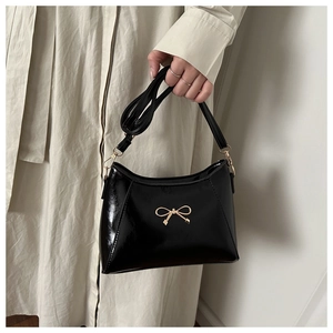 Detail of glossy black handbag featuring gold bow hardware and adjustable strap