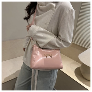 Close-up of pink crescent handbag with gold bow hardware on a stylish shoulder bag