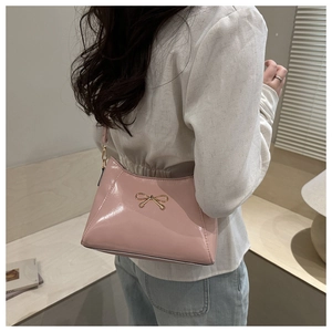 Detail of pink glossy shoulder bag with golden metal bow on a female model shoulder