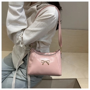 Pink crossbody bag with golden bow detail shown on a model in a minimal setting