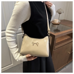 Close-up of beige glossy leather shoulder bag with a gold metal bow and adjustable strap