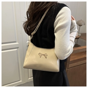 Close-up of a cream PU leather shoulder bag with a gold metal bow on a model