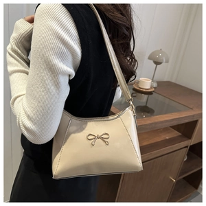 Detail of a creamy white crescent bag with a gold bow buckle on a wooden cabinet