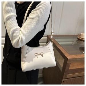 Close-up of white bow shoulder bag with gold hardware worn in a chic urban setting
