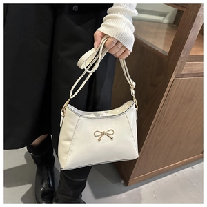 Close-up of cream handbag featuring a decorative gold bow and adjustable shoulder strap