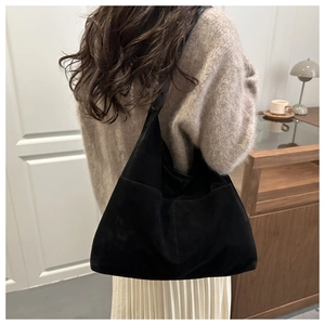 Detail of a large black suede hobo shoulder bag shown on shoulder in a cozy cafe setting