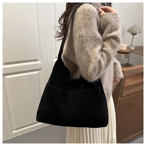Detail of a large black suede tote bag with a side pocket worn by a model in a minimalist style