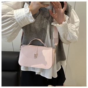 Detail of light pink faux leather crossbody bag with golden U-shaped buckle and wide strap