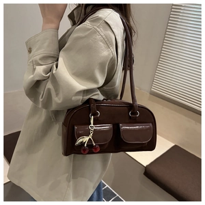 Detail view of brown suede shoulder bag featuring decorative pockets and cherry charm