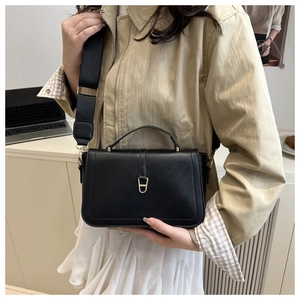 Detail of minimalist black leather handbag with golden lock and adjustable wide strap