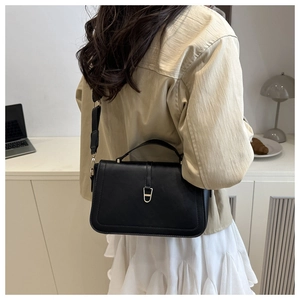 Detail of a black leather crossbody bag with golden buckle on a casual white skirt outfit