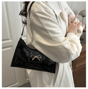 Elegante borsa sottobraccio in vernice nera con fiocco dorato indossata da modella
