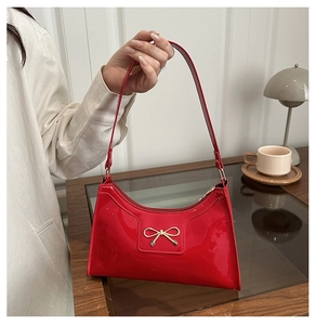 Dettaglio della borsa a spalla in pelle verniciata rossa con fiocco in metallo dorato