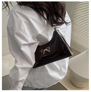 Borsa a spalla in pelle verniciata lucida con fiocco dorato indossata da modella in luce soffusa