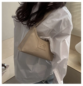 Dettaglio della fibbia a fiocco dorato sulla borsa a spalla in pelle beige lucida