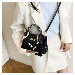 Détail du sac à main noir en texture crocodile avec fermoir doré et foulard élégant