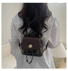 Detail of a mini chocolate brown patent leather backpack with gold clasp and drawstring