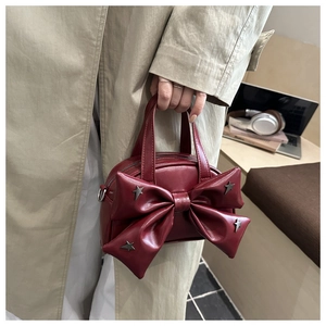 Dettaglio borsa a mano bordeaux con fiocco e borchie a stella in un contesto urbano