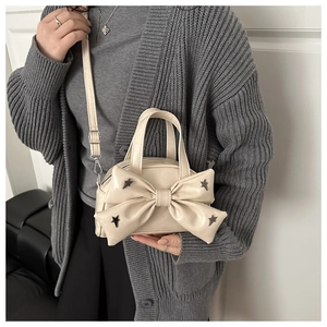 Borsa beige con grande fiocco e borchie a stella indossata dalla modella per scala