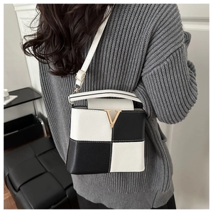 Detail of crossbody bucket bag featuring black and white checkerboard pattern and V-clasp