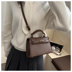 Detailed view of a brown leather trapezoid bag with gold hardware worn by a model