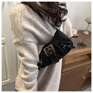 Detail of black canvas shoulder bag with large silver metal buckle worn by model