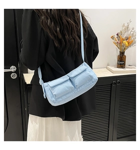 Dettaglio borsa in nylon azzurro con doppie tasche anteriori su modella di profilo