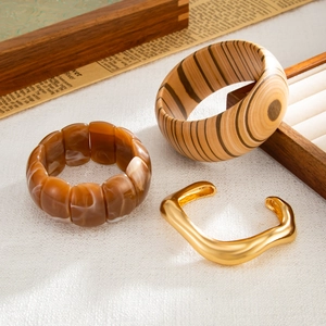 Dettaglio del bracciale in legno, del bracciale in resina ambra e del polsino dorato