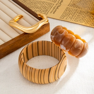 Dettaglio di un set di bracciali in legno, metallo dorato ondulato e resina ambrata