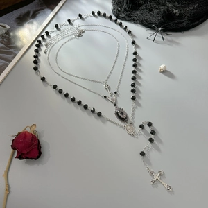 Dettaglio collana gotica multistrato con croce, teschio e catena di perline nere a rosario