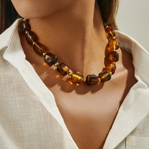 Dettaglio di una collana con perle in resina ambra e distanziatori dorati indossata da modella