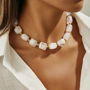 Dettaglio di perle in resina bianca e sfere metalliche dorate sulla collana