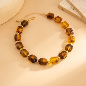 Dettaglio delle perle in resina ambra con accenti dorati e chiusura a moschettone