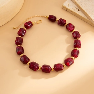 Dettaglio di perline di resina rosso scuro e distanziali dorati sulla collana regolabile