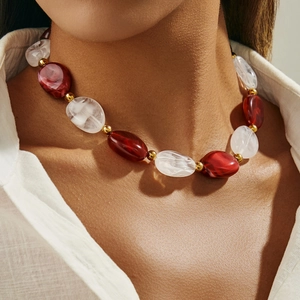 Dettaglio macro di perline in resina marmorizzata bordeaux e bianca su collana dorata